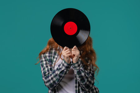 Positive red haired woman with vinyl record disc on blue. Hobby, music lover, collection, nostalgia lifestyleの写真素材