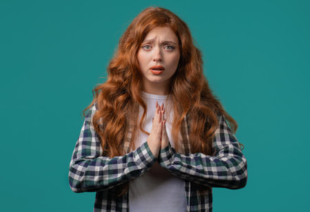 Young woman praying, begs to apologize her, she is guilty. Blue background. Hopeful prayer girl...