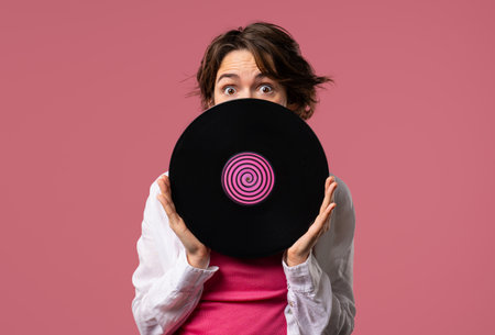 Positive short haired woman with vinyl record disc on pink. Hobby, music lover, collection, nostalgia lifestyleの写真素材