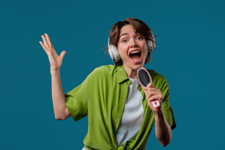 Woman singing, dancing with hair brush instead microphone on Blue background. Lady having fun, listening to music, karaoke, dreams of being celebrity.の写真素材