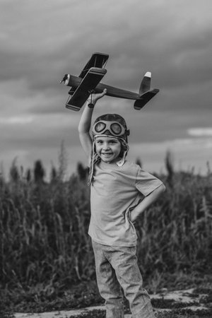 Smiling Interested Child Boy in Pilot Helmet Playing With Wooden Airplane.の写真素材