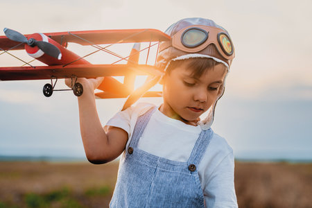 Smiling Interested Child Boy in Pilot Helmet Playing With Wooden Airplane.の写真素材