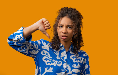 African teen girl with dislike sign. Stylish lady showing thumbs-down on yellowの写真素材