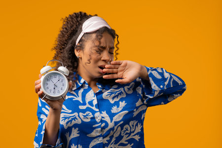 Woken up by alarm clock sleepy young african woman. Yellow background, lazinessの写真素材