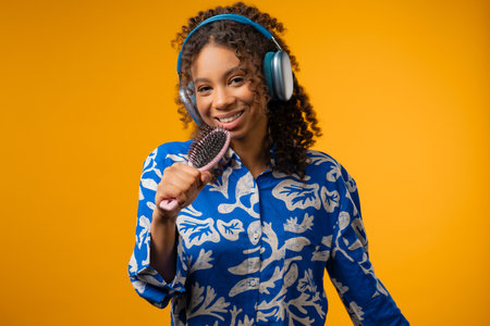 African teenager girl singing, dancing with hairbrush as microphone on yellowの写真素材