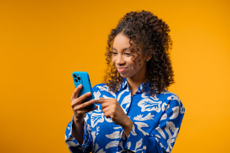 Young adult african woman surfing internet smartphone. Girl with smile on yellowの写真素材