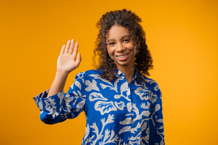 Friendly african eoman waving hand - Hello, Hi, Salute. Greetings on yellowの写真素材