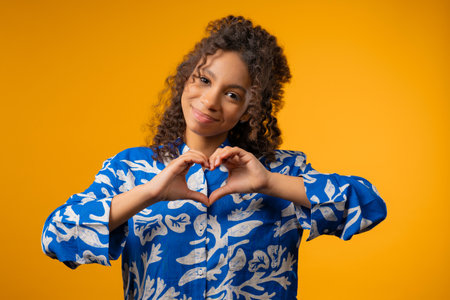 Teenager zoomer girl showing sign of shape heart. Positive lady on yellow. Love.の写真素材