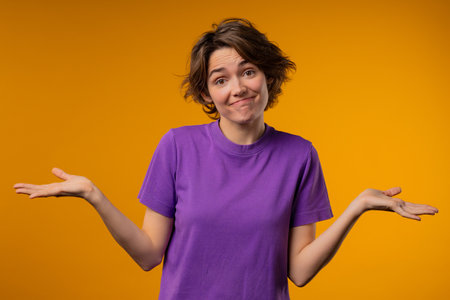 Confused pretty woman, shoulders up - cant help, makes gesture of I dont know. Difficult question, puzzled lady on yellow backgroundの写真素材