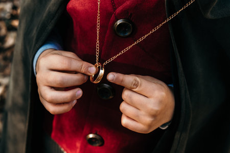 Unrecognizable child cosplayer in hobbit cape costume holding and wants to wear golden ring. Fantasy journey, halloween, fellowship cosplayの写真素材
