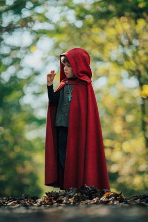 Cute cosplayer hobbit kid in cape costume in forest watching gold ring. Fantasy journey in fairytale wonderland, halloween, cosplayの写真素材