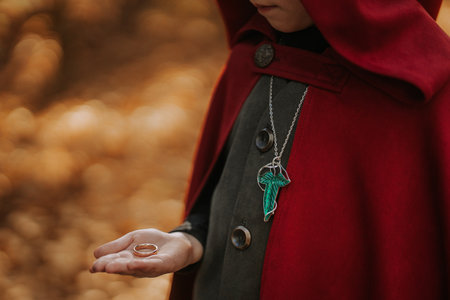 Cute cosplayer hobbit kid in cape costume in forest watching gold ring. Fantasy journey in fairytale wonderland, halloween, cosplayの写真素材