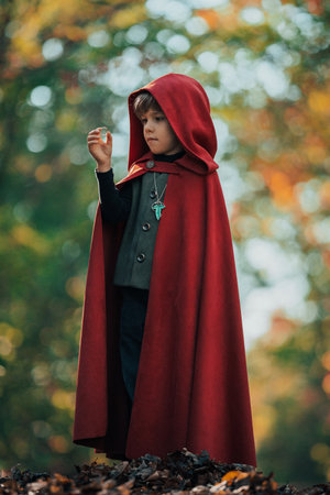 Cute cosplayer hobbit kid in cape costume in forest watching gold ring. Fantasy journey in fairytale wonderland, halloween, cosplayの写真素材