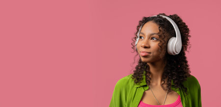 African woman listening music, enjoying with headphones on Pink, online player, copy spaceの写真素材