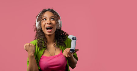 Young african teenager girl gamer playing and winning online video game on console with joystick, copy space, modern technology. E-sport, hobby, streamingの写真素材