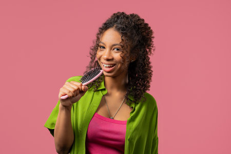 African teenager girl singing, dancing with hairbrush as microphone on pinkの写真素材