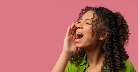 Portrait of young woman shouting, holding hand near open mouthの写真素材