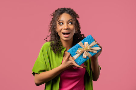 Happy young african woman with gift box on pink background. Positive girl smiling, present in hands. Offer surprise for youの写真素材