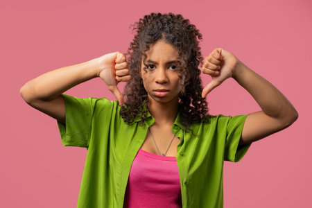 African teen girl with dislike sign. Stylish lady showing thumbs-down on pinkの写真素材