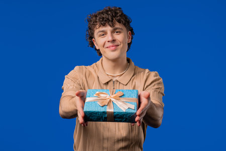Man gives gift box by hands to camera on blue background. Guy smilingの写真素材