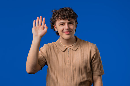 Friendly curly haired young Man Waving Hand - Hello, Hi, Salute. Greetings.の写真素材