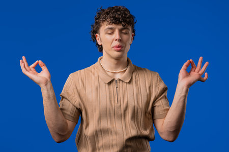 Tranquil curly man relaxing, meditating, refuses stress. Breathes deeply on blueの写真素材