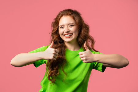 Positive woman with hand sign like, thumbs up gesture. Lady on pink backgroundの写真素材