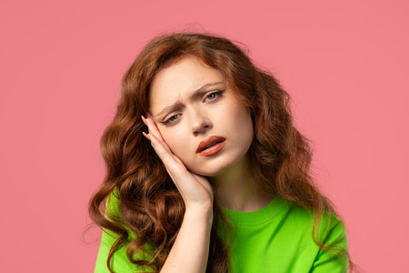 Portrait of suffering woman having headache, pink studio. Girl hands on headの写真素材