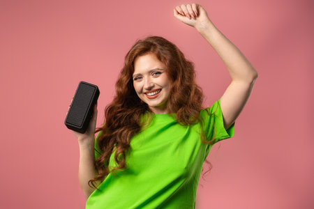 Young woman dancing, listening to music by wireless portable speaker on pinkの写真素材