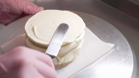 Pastry chef leveling cake sides with cream. Confectioner working with spatula.の写真素材