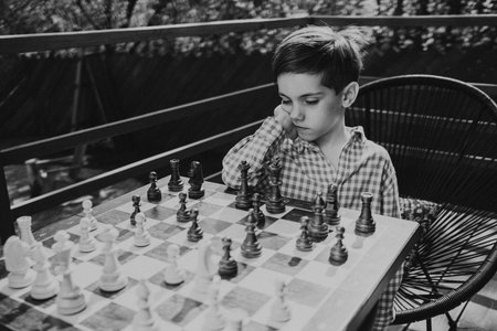 Pensive little boy playing chess game, considering next move. KIds competition