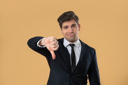 Businessman in suit giving thumbs down dislike with disapproving look on beige
