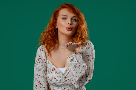 Playful ginger woman sends air kiss with gentle hand motion, warm emotional toneの写真素材