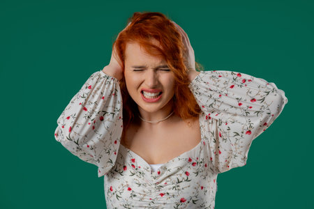Irritated Young Red-haired Woman Covering Ears Ignoring On Green. Noise, Shouts.の写真素材