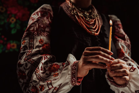 Ukrainian woman in traditional clothing holding candle in dark room interiorの写真素材