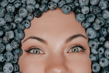 Woman face in fresh ripe blueberries. Young girl covered with acai berries.の写真素材