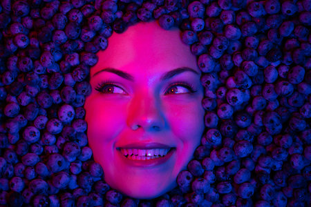 Woman face in fresh ripe blueberries. Young girl covered with acai berries.の写真素材