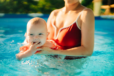 Mother teaching baby girl to swim in bright indoor home pool, bonding momentの写真素材