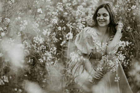 Retro style young woman in black and white photo sitting in rapeseed field