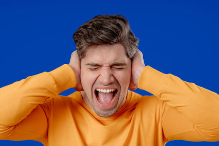 Man in yellow reacts with frustration by blocking out noise or unwanted information. Stress,...