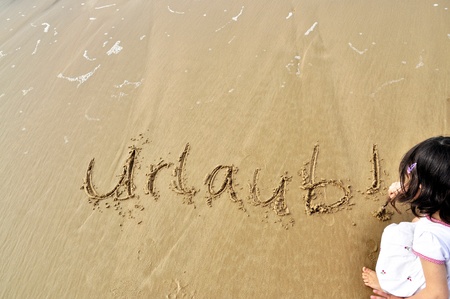 Little girl writing the word Urlaub! (German for vacation) in the sandの写真素材