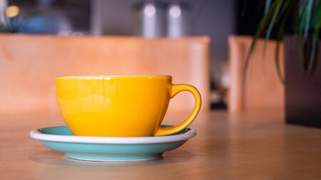 Coffee mug on the background of the cafe, standing on a wooden table. Green plant in the corner.