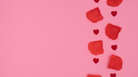Small red hearts and red rose petals lying on a pink background.の写真素材