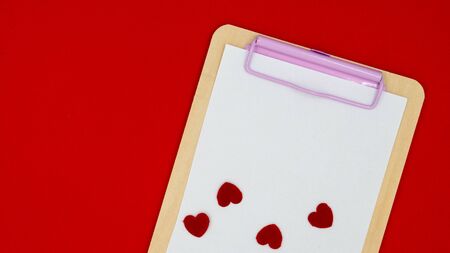 Click Board with a white blank card and black hearts, lying on a red background.の写真素材