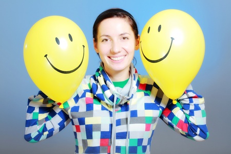 girl with two yellow smiley balloons against blueの写真素材
