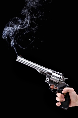 hand holding a revolver with smoking barrel, against black backgroundの写真素材