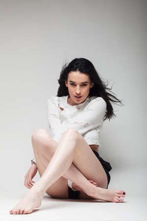 full body shot of beautiful black haired lady sitting on the ground  bare feetの写真素材