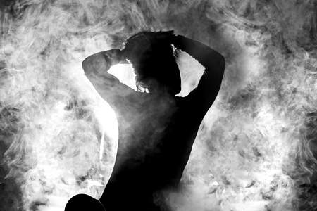 silhouette of a girl streching in sitting position, white smoke in the backgroundの写真素材