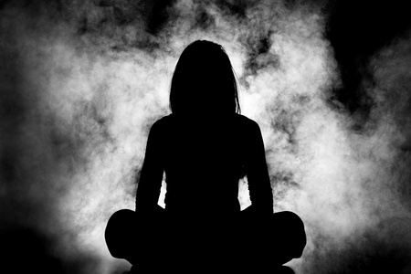 silhouette of a girl meditating against white smoke backgroundの写真素材