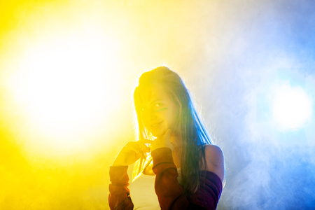 young party girl dancing against yellow and blue backlit smokeの写真素材